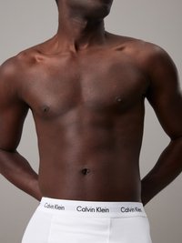 White Calvin Klein boxer briefs with black waistband logo, worn by a person with a dark skin tone and visible chest and abdomen.