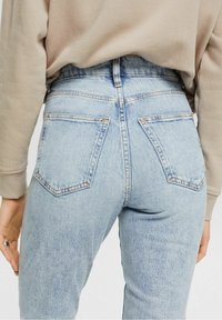 Un jean en denim léger bleu clair à taille haute avec un léger délavage, deux poches arrière et une couture contrastante, associé à un sweat-shirt beige.