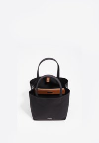 Zwarte canvas draagtas met twee handvaten, voorzien van een bruine ritszak aan de binnenkant. Minimalistisch ontwerp met zilveren hardware en logo aan de onderkant.