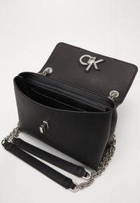 Sort læderhåndtaske med sølvkæde og rem. Har et fremtrædende sølv CK-logo på klappen og indvendige rum til opbevaring.