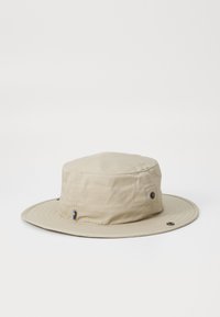 Chapeau seau beige avec un large bord plat et une couronne arrondie. Présente des détails de couture et un petit accent avec des couleurs bleu et jaune.