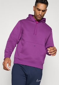 Lilla hoodie med kangaroo-lomme, snoretræk i huen og logodetalje i mørkeblå. Blødt stof med afslappet pasform og ribbede manchetter.