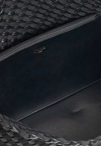 Black woven handbag with a zipper closure. Interior features smooth leather lining with a small logo embossed. Textured exterior.