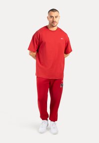 Camiseta de algodón roja de manga corta con un logo en el pecho, combinada con pantalones jogger rojos a juego que presentan un parche y zapatillas blancas.