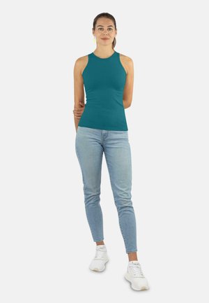Türkises ärmelloses Oberteil mit taillierter Passform, kombiniert mit hellblauen Jeans und weißen Turnschuhen, die einen lässigen, geschichteten Look kreieren.