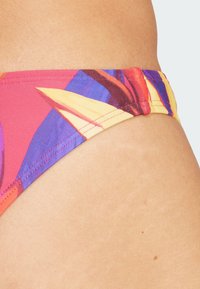 Fondo bikini colorato con un motivo floreale in tonalità di rosa, giallo e viola, realizzato in un materiale liscio e elastico con cuciture pulite.