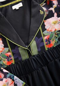 Abito nero a fiori con colletto con piping verde, chiusura a bottoni e vita elastica. Il tessuto presenta vivaci motivi floreali.