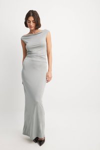 Langes graues Kleid aus weichem, dehnbarem Material mit weitem Rundhalsausschnitt und taillierter Form. Es hat eine glatte Oberfläche und ein bodenlanges Design. Schwarze Absätze.