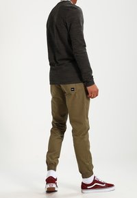 Dunkelgraues Langarmshirt, khakifarbene Jogginghose mit elastischen Bündchen, rote und weiße Sneakers, mit sichtbarem Markenetikett auf der Hose.