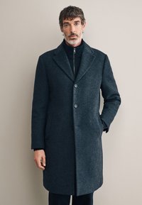 Cappotto in lana grigio scuro con colletto a risvolto con tacca, chiusura a due bottoni e tasche laterali, tessuto strutturato e vestibilità sartoriale.