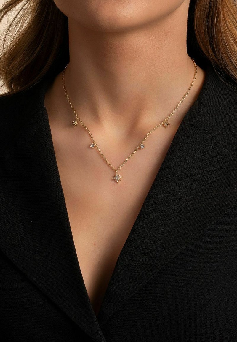 Guldhalsband med stjärnformade accenter och gnistrande ädelstenar, vilande på en svart klädnad. Enkelt, elegant design.