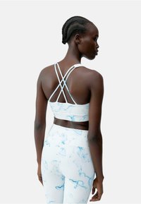 Witte sportbeha met een blauw marmerpatroon, voorzien van dunne crisscrossbandjes. Gecombineerd met bijpassende legging die een soepele textuur toont.