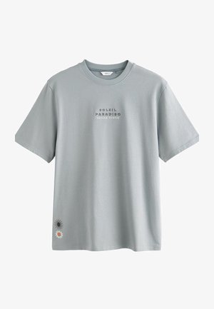 Heledad hallide puuvillane T-särk lühikeste käistega, millel on "SOLEIL PARADISO TEXAS AUSTIN" tekst ja päikese ning lille graafika ääres.