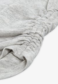 Tessuto grigio chiaro con una superficie morbida, caratterizzato da cuciture arricciate lungo il bordo. Il tessuto è liscio e leggermente elastico.