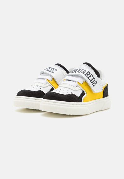 Sneaker con una parte superiore in suede nero e pelle bianca, dettagli in pelle gialla, lacci bianchi e una strap in velcro con il nome del marchio.