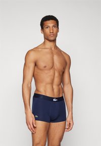 Boxers em azul marinho feitos de um tecido suave, com uma cintura larga decorada com logótipo e marcação em contraste na perna esquerda. Design ajustado.