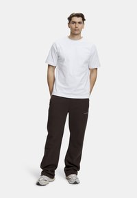 Vit bomull t-shirt i kombination med mörkbruna sweatpants med fickor. Skorna är ljusgrå med en strukturerad design. Övergripande avslappnad passform.