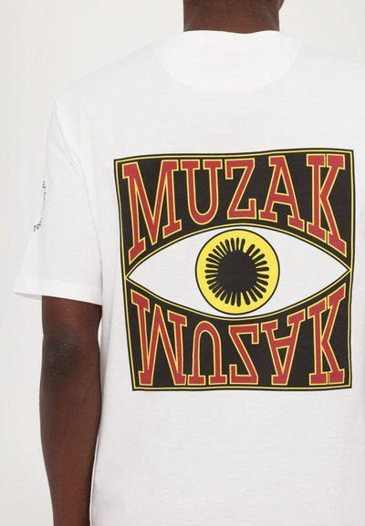 Valge lühikeste varrukatega T-särk, millel on suur graafiline disain, kus on kollane ja must silmasümbol ning punastes tähtedes ülalt alla kirjutatud "MUZAK".
