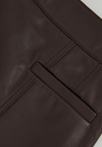 Giacca in pelle marrone con una texture liscia, cuciture angolari e una tasca inserita sul lato sinistro superiore.