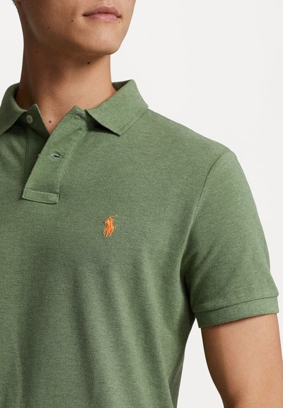 Polo verde de tejido texturizado, con un cuello clásico, botonera de dos botones y un logotipo bordado en naranja en el pecho.