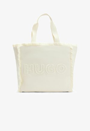 Tragetasche aus cremefarbenem Stoff mit ausgefransten Kanten, mit dem geprägten Schriftzug "HUGO" auf der Vorderseite. Robuste Henkel zum Tragen.
