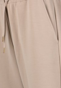 Beige joggers met een gladde textuur, elastische tailleband, trekkoord met gouden accenten en zijzakken.