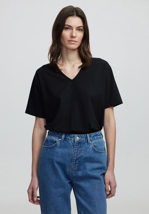 Camiseta negra de cuello en V y mangas cortas, fabricada en tejido suave. Combinada con jeans de mezclilla azul de cintura alta con un diseño clásico de cinco bolsillos.
