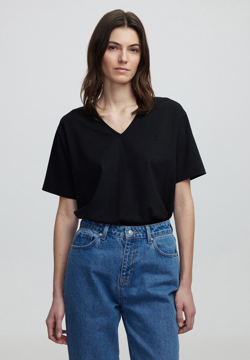 T-shirt nero con scollatura a V e maniche corte, realizzato in tessuto morbido. Abbinato a jeans in denim blu a vita alta con un classico design a cinque tasche.