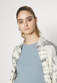 Ilga rankovė, mygtukais užsegama marškinėlių palaidinė su pilkai balta tye-dye raštu, uždėta ant šviesiai mėlynos trumpa rankove palaidinės. Minkšta medvilnės medžiaga, laisvo silueto.