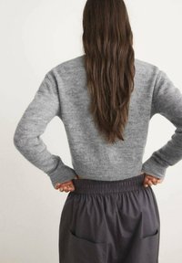Grijze cropped trui gemaakt van zachte stof met lange mouwen, gecombineerd met donkergrijze hoge taille broek met zijzakken.