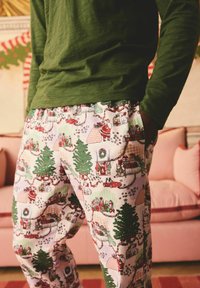 Bomullspyjamasbyxor med ett festligt mönster som har julgranar, paket och figurer. Ljus bakgrund med gröna och röda akcentfärger.