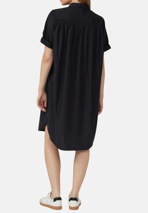 Abito shirt nero con maniche corte arrotolate, schiena arricciata e spacchi laterali, abbinato a sneakers bianche con accentuazione nera sul tallone.