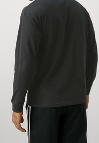 Long-sleeve black t-shirt made of cotton, featuring a simple design and a relaxed fit, paired with dark athletic shorts with white stripes.