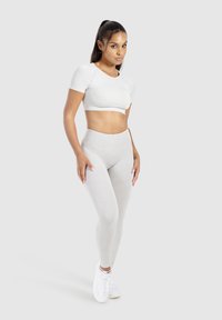Top atletico bianco a maniche corte e leggings grigi chiari a vita alta, texture liscia, abbinati a sneaker bianche. Design semplice, senza motivi visibili.