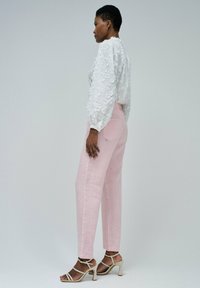 Blusa blanca bordada de flores con mangas abullonadas, combinada con pantalones de tiro alto rosa claro y tacones beige con tiras.