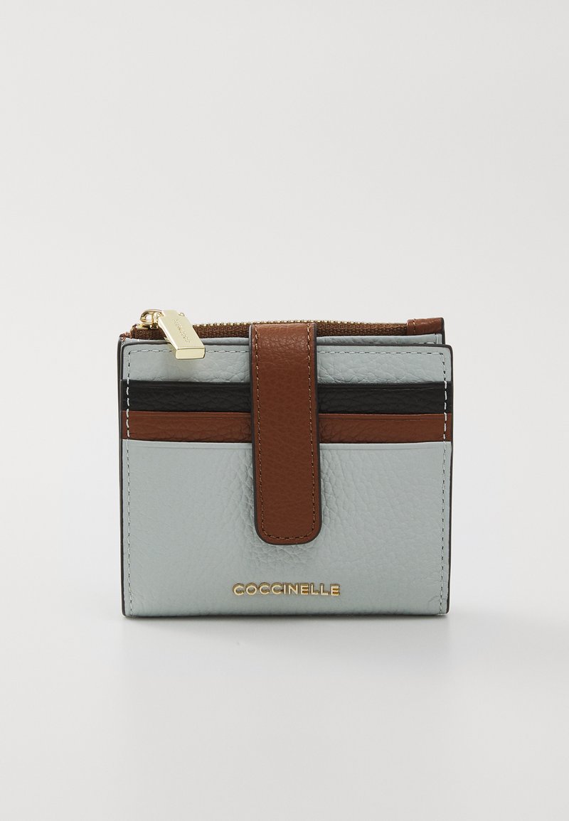 Kompaktní peněženka ve světle modré texturované kůži, s hnědými a černými pruhy. Zlaté kovové detaily s logem na přední straně a zipovým uzávěrem.