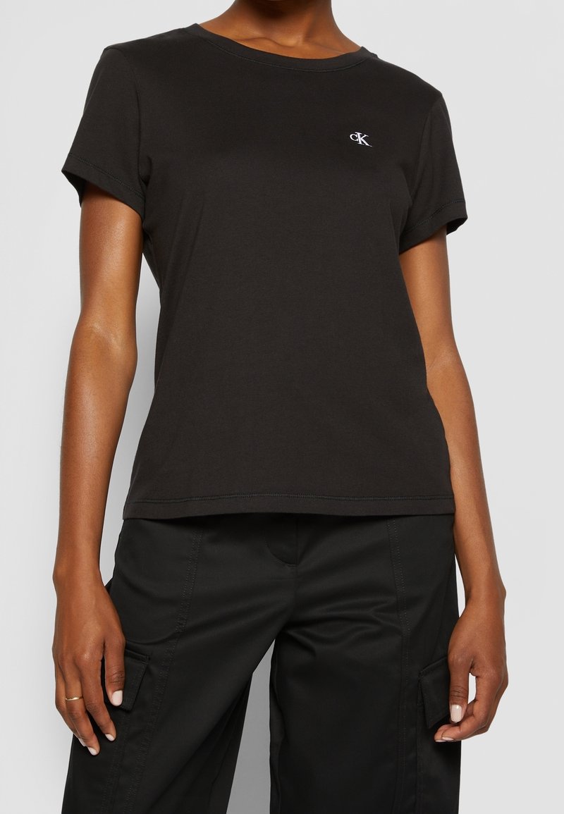 Musta puuvillainen lyhythihainen T-paita, jossa on pyöreä kaula-aukko ja pieni brodeerattu logo rinnassa. Sujuva rakenne ja rento istuvuus.