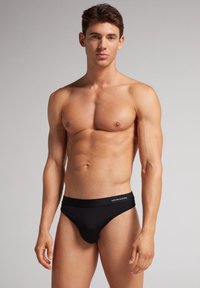 Slip noir avec une ceinture élastique arborant un logo, fabriqué dans un tissu lisse et extensible. Conçu pour une silhouette ajustée.