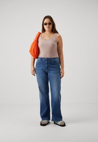 Top sem mangas com riscas em azul, laranja e branco; jeans azul claro com corte descontraído; mala laranja acolchoada; óculos de sol; sandálias rasas.