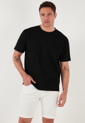 Tricou scurt negru cu mânecă scurtă, realizat din bumbac moale. Are guler rotund și o croială lejeră, asortat cu pantaloni scurți albi răsuciți.