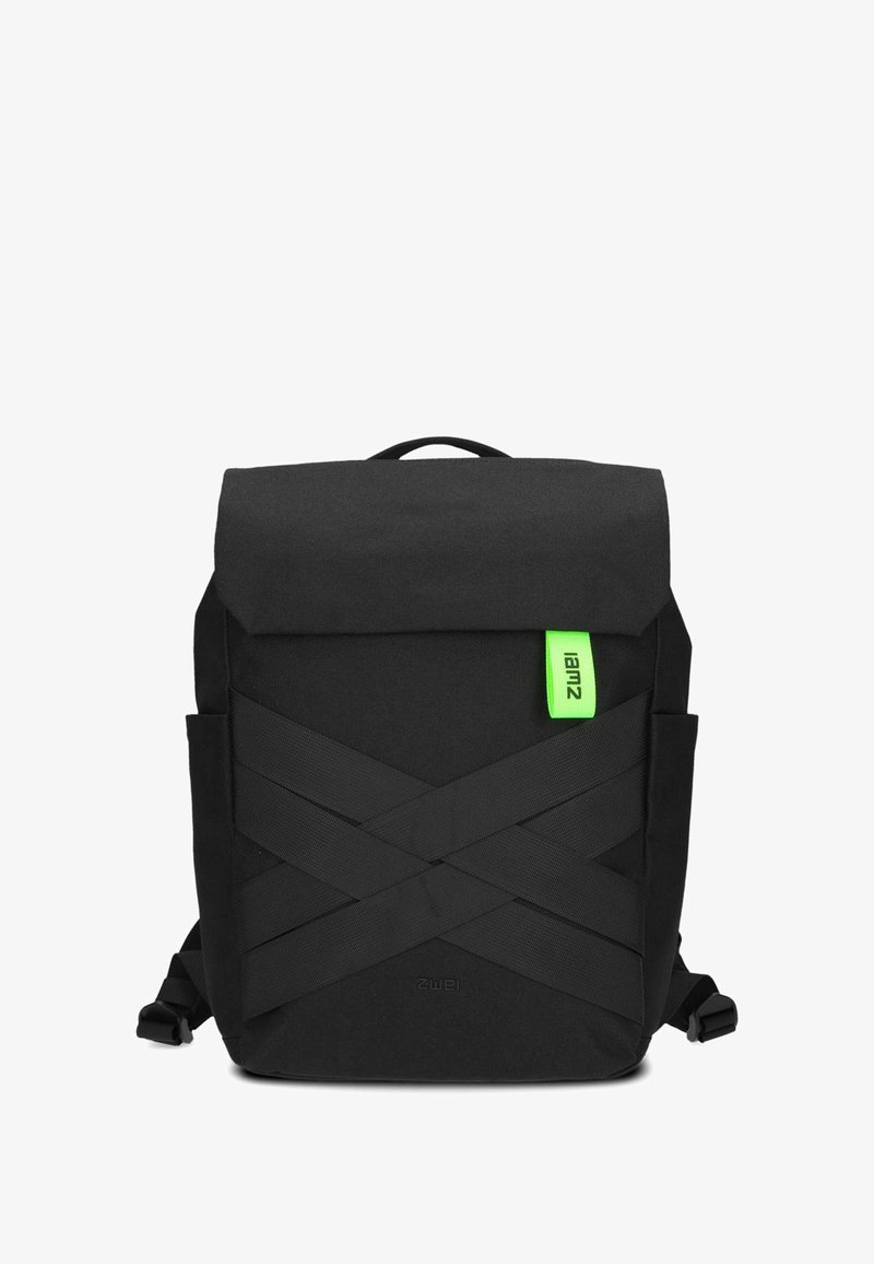 Sac à dos noir avec un rabat, doté d'une étiquette verte vif et de détails de sangle diagonaux. Fabriqué en tissu durable avec des poches latérales.