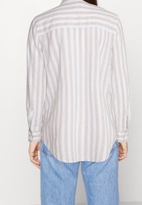 Lightweight, long-sleeve shirt featuring a vertical stripe pattern in beige and white, with a curved hem and buttoned cuffs.