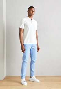 Hvid kortærmet polo med lys blå chinos og hvide sneakers. Glat stof, enkelt design, neutral farveskema.