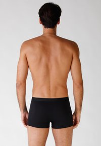 Boxer in cotone nero con una texture liscia, caratterizzati da una fascia morbida. Vista da dietro, che mette in mostra il torso del modello senza calzature.