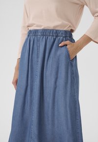Denim maxi suknja s elastičnom pasicom, dva bočna džepa i glatkom teksturom. Svijetloplava boja s suptilnom varijacijom nijanse.