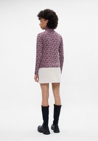 Top de manga larga y ajustado con un patrón floral rosa, combinado con una falda mini de color claro y botas negras de caña alta con tacón grueso.