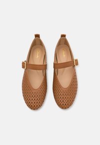 Zapatos de cuero marrón perforados con puntera redondeada y una correa con hebilla a lo largo del empeine. Forro interior suave y suela plana.