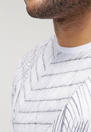 Weißes T-Shirt mit einem geometrischen schwarzen Linienmuster, rundem Ausschnitt und kurzen Ärmeln. Weiche Textur, Nahaufnahme des Oberkörpers.