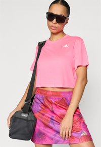 Ροζ cropped t-shirt με λογότυπο, φούστα με λουλουδάτο σχέδιο σε ροζ και μωβ αποχρώσεις και μικρή μαύρη τσάντα ώμου με λουράκι.