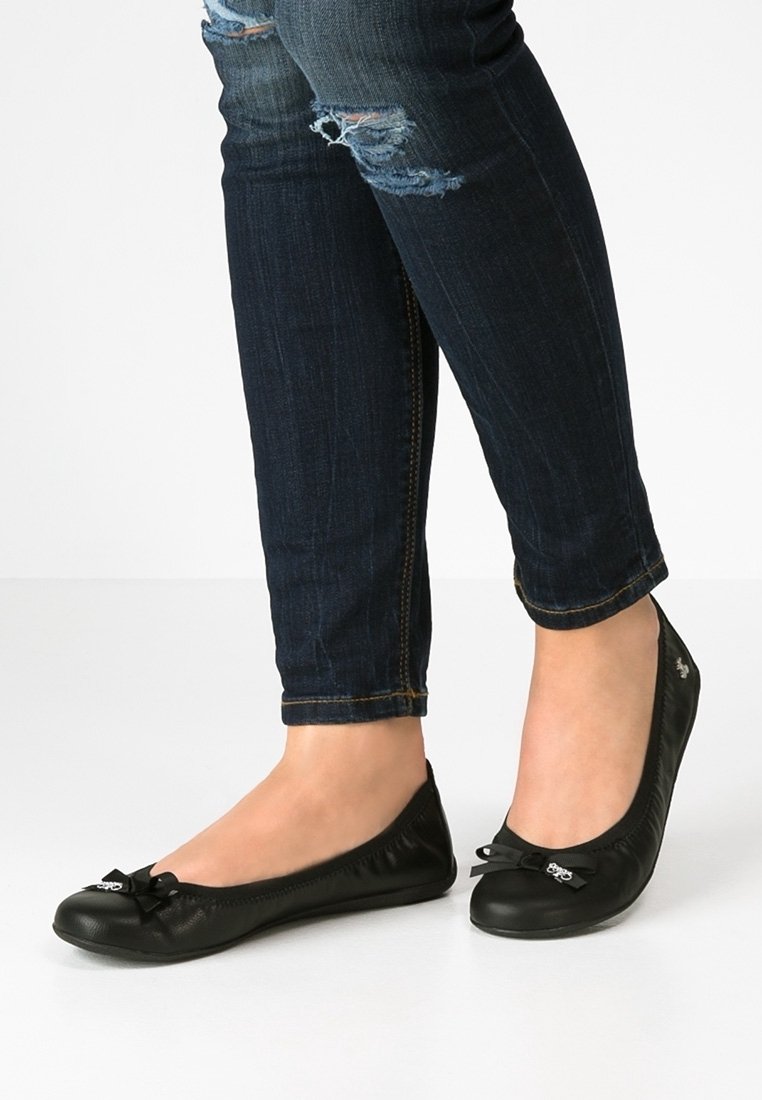 Svarta platta skor med rund tå, mjukt lädermaterial och en liten rosettdetalj fram. Bärs med mörka jeans.